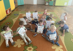 Dzieci siedzą na dywanie z dyplomami