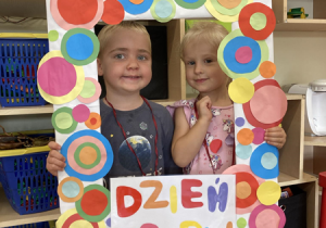 Dziewczynka i chłopiec pozują do zdjęcia trzymając fotoramkę z napisem „Dzień Kropki”