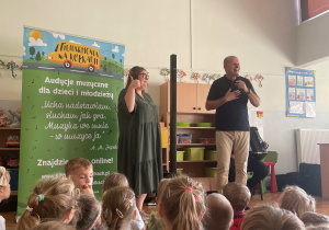 Pani Nauczycielka stoi na środku sali i pokazuje kciuk w górę