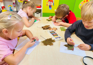 Dzieci wykonują prace plastyczną odrysowując liście