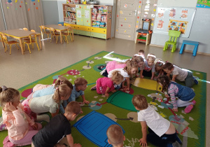 Dzieci siedzą na dywanie i biorą udział w zajęciach z segregacji śmieci