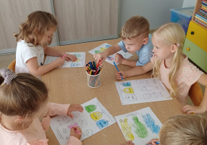 Dzieci siedzą przy stoliku i wykonują kartę pracy związaną z segregacja śmieci