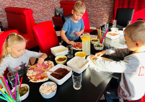 Dzieci dekorują pizzę ulubionymi dodatkami
