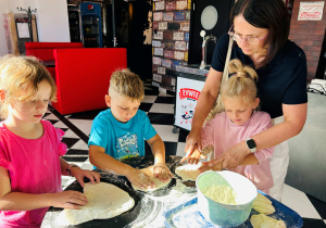 Dzieci z pomocą nauczycielki ugniatają pizzę