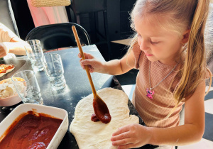 Dziewczynka przygotowuje pizzę nalewając na ciasto sos
