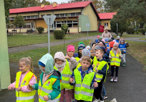 Dzieci ubrane w kamizelki spacerują po placu przedszkola