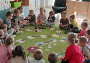 Dzieci siedzą na dywanie i wspólnie uczestniczą w zabawie z włóczką