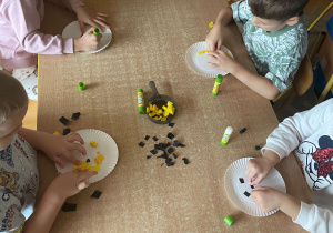 Dzieci siedzą przy stolikach i wykonują pracę plastyczną