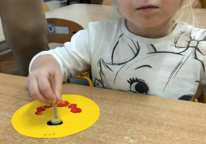 Dziewczynka wykonuje pracę plastyczną- uśmiechniętą buźkę