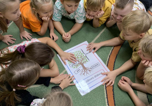 Dzieci leżą na dywanie i poznają budowę drzewa z planszy dydaktycznej