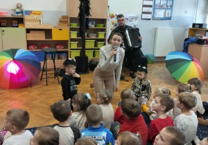 Dzieci przebrane za koty siedzą obok pani, która śpiewa