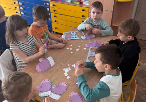 Dzieci wykonują prace plastyczna. Nawlekają włóczkę na rękawiczki