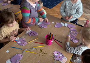 Dzieci wykonują prace plastyczna. Nawlekają włóczkę na rękawiczki