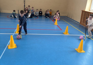 Dzieci biorą udział w konkurencji sportowej tocząc piłkę