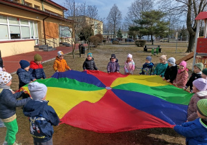 Dzieci bawią się kolorową chustą animacyjną na świeżym powietrzu.
