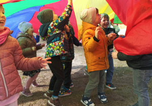 Kolorowa chusta animacyjna falująca podczas zabawy dzieci na zewnątrz.