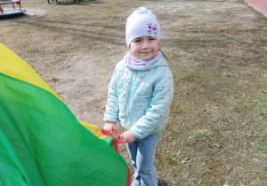 Dziewczynka bawi się kolorową chustą animacyjną na świeżym powietrzu.