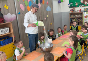 Dzieci obserwują piekarza wsypującego mąkę do miski