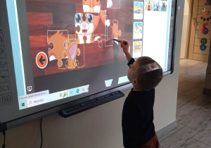 Chłopiec układa puzzle na tablicy multimedialnej