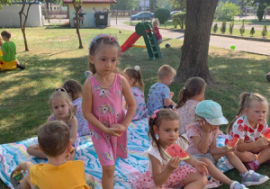 Dzieci siedzą na kocu i jedzą arbuza