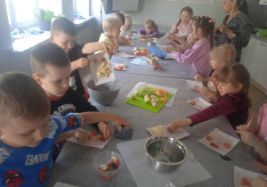 Dzieci dodają ulubione owoce do sałatki.