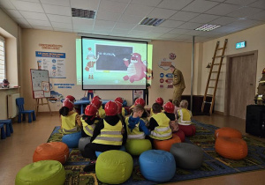 Dzieci w strojach strażackich oglądają film edukacyjny