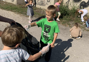 Dzieci wyrzucają zebrane śmieci do worka na śmieci