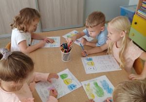 Dzieci siedzą przy stoliku i wykonują kartę pracy związaną z segregacja śmieci
