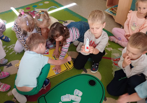 Dzieci siedzą na dywanie i biorą udział w zajęciach z segregacji śmieci