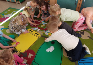 Dzieci siedzą na dywanie i biorą udział w zajęciach z segregacji śmieci