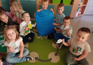 Dzieci siedzą na dywanie i biorą udział w zajęciach z segregacji śmieci