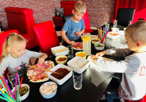 Dzieci dekorują pizzę ulubionymi dodatkami
