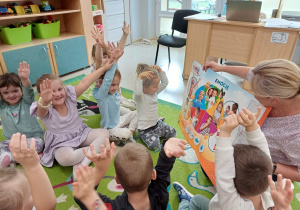 Dzieci siedzą na dywanie wraz z nauczycielką, która rozmawia z nimi na temat emocji
