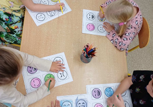 Dzieci siedzą przy stoliku i wykonują pracę plastyczną na temat emocji