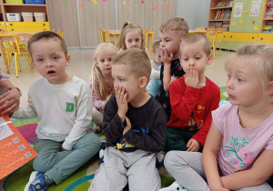 Dzieci siedzą na dywanie i pokazują konkretne emocje