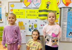 Dziewczynki pozują do zdjęcia z tablicą dotycząca Dnia Odblasku