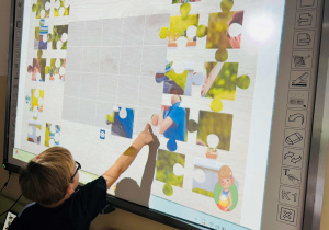 Chłopiec układa puzzle na tablicy interaktywnej
