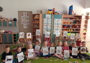 Dzieci siedzą na dywanie i pozują do zdjęcia z napisem z okazji Dnia Zwierząt
