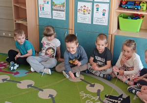 Dzieci siedzą na dywanie i wspólnie uczestniczą w zabawie z włóczką