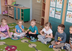Dzieci siedzą na dywanie i wspólnie uczestniczą w zabawie z włóczką