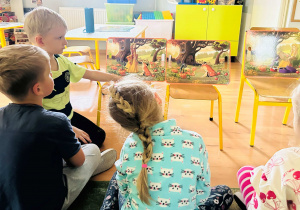Dzieci siedzą na dywanie i słuchają bajki oglądając obrazki