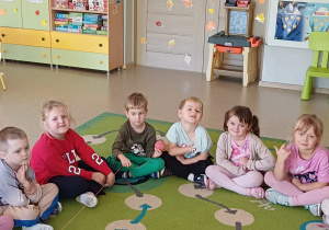 Dzieci siedzą na dywanie i wspólnie uczestniczą w zabawie z włóczką
