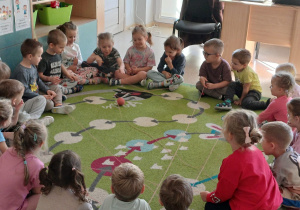 Dzieci siedzą na dywanie i wspólnie uczestniczą w zabawie z włóczką