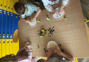 Dzieci siedzą przy stolikach i wykonują pracę plastyczną