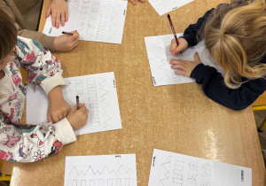 Dzieci ćwiczą pisanie szlaczków na kartach pracy