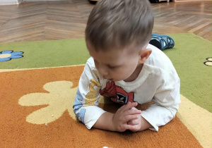 Chłopiec leży na dywanie i zbiera watę