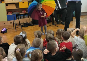 Dzieczynka stoi na środku z parasolem obok pana Maćka