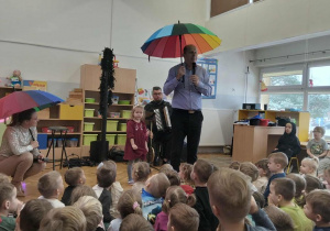 Dziewczynka stoi na środku obok pana Maćka i pani z parasolami