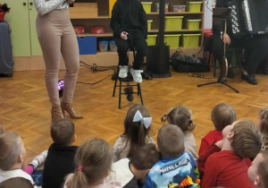 Chłopiec przebrany za kominiarza siedzi na stołku obok pani, która śpiewa