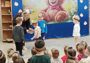 Nauczycielka częstuje dzieci żelkami za udział w konkursie